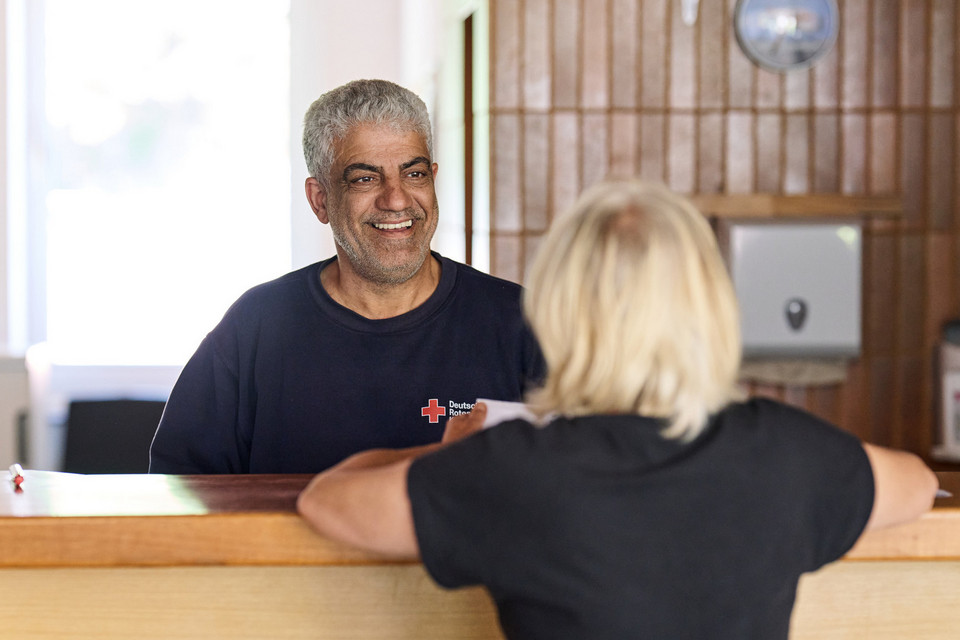 Ein Mitarbeiter des Roten Kreuzes und eine Frau sitzen sich in einer Beratungssituation an einem Tisch gegenüber.