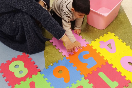 Ein Kind und eine erwachsene Person knien auf dem Boden und machen zusammen ein Puzzle, dessen große Teile Ziffern 0 bis 8 sind.