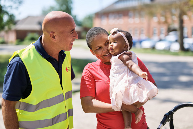 DRK Mitarbeiter begrüßt eine Frau mit kleinem Kind vor einer Unterkunft